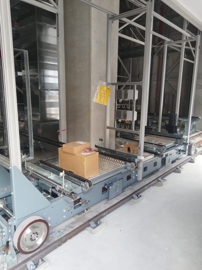 Rail-guided transfer car with chain conveyor deck in front of the high-bay racking